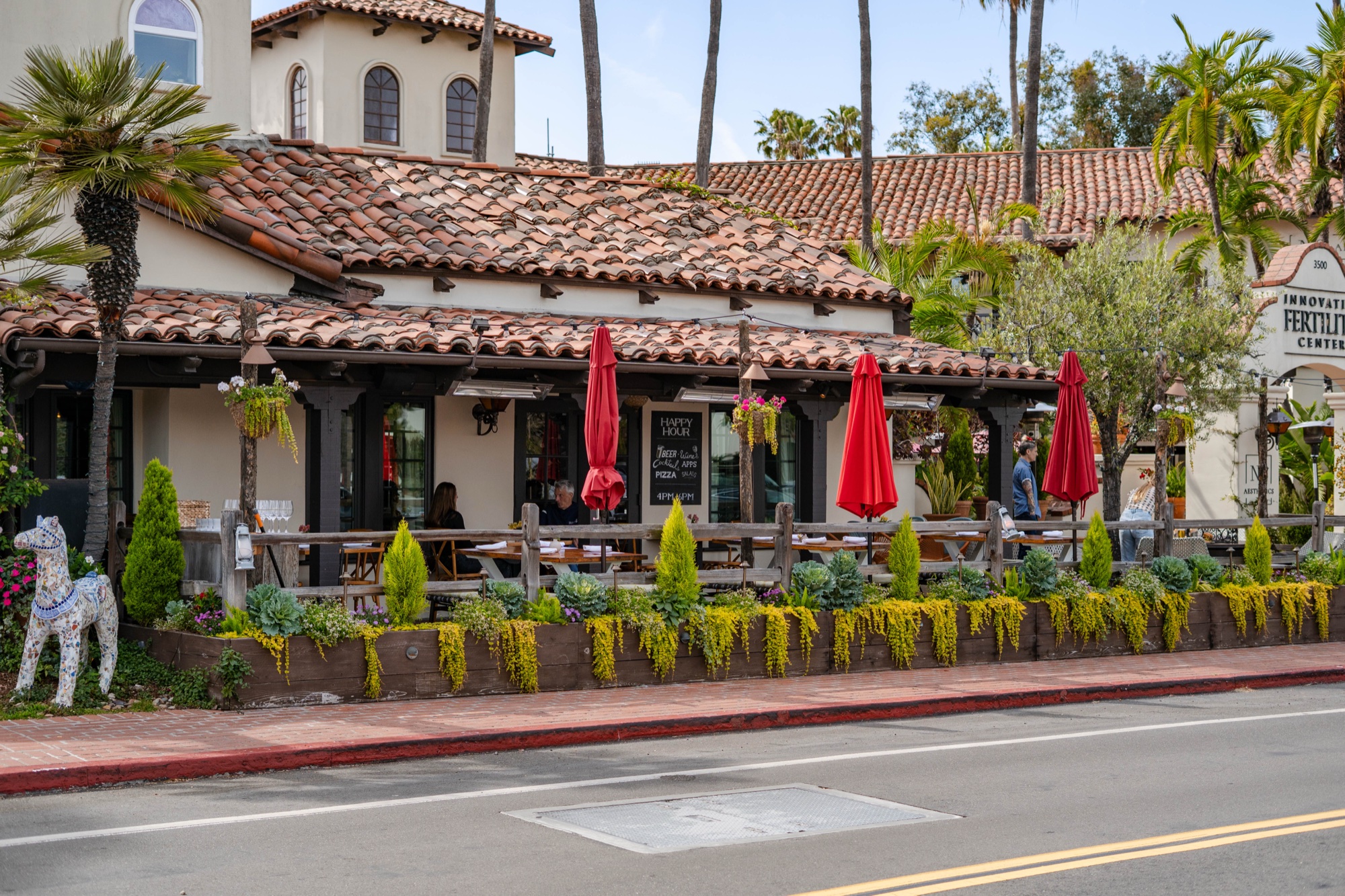 Red umbrellas and tables on the streetside Front Porch at Tin Roof Bistro