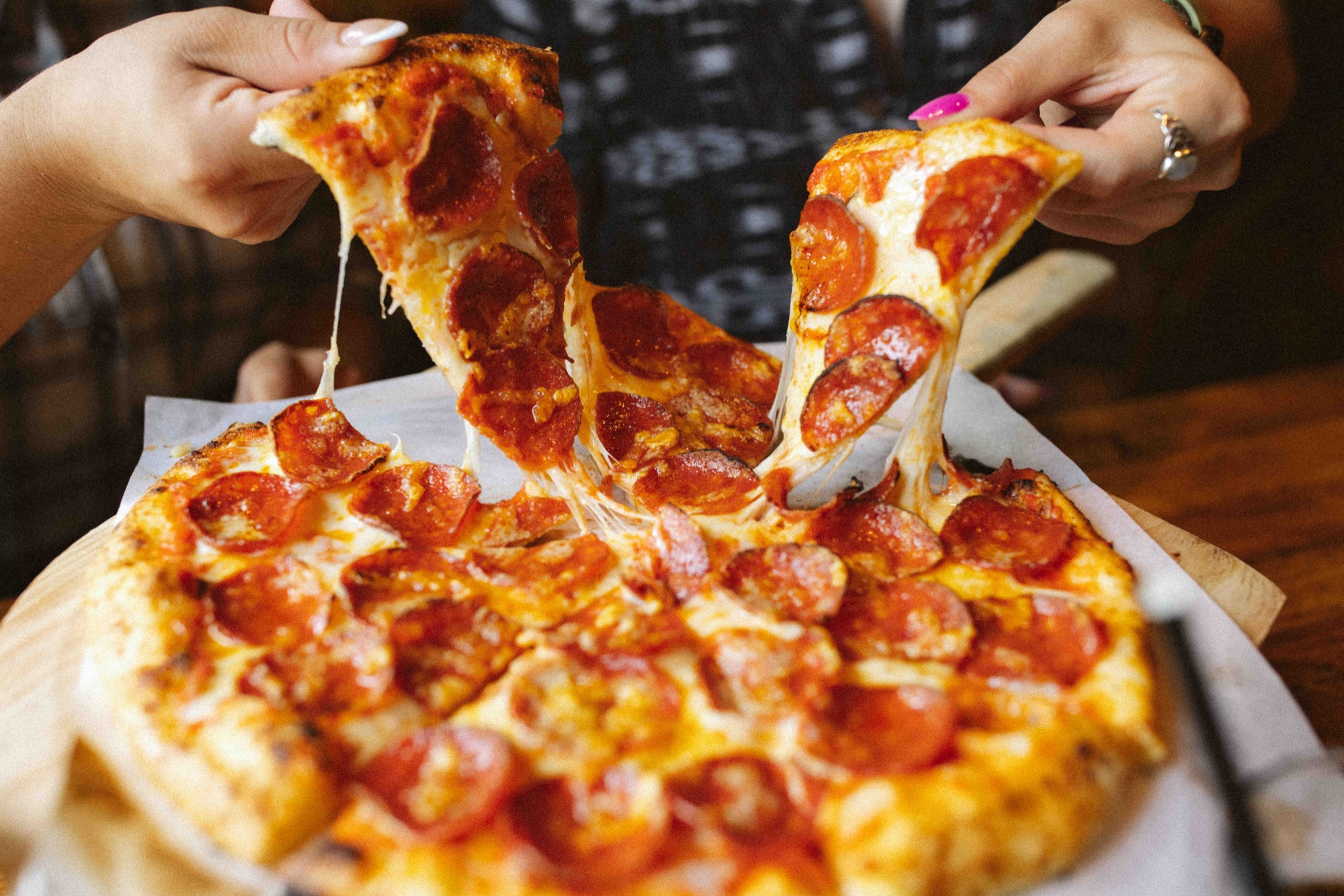 Hands pulling a cheesy slice from a wood-fired pepperoni pizza at Tin Roof Bistro