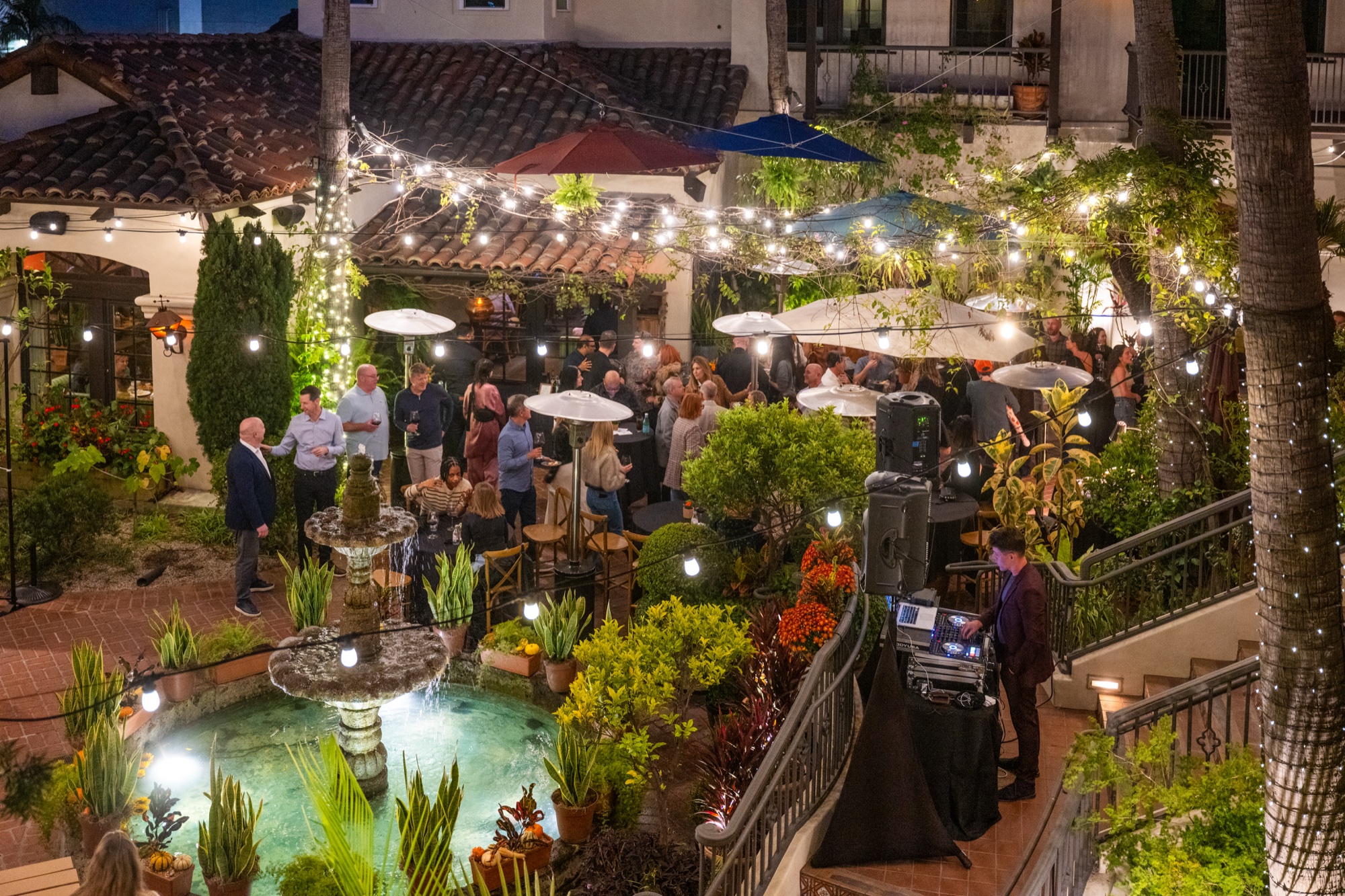 A private event in the string-lit Tin Roof Bistro courtyard at dusk, guests mingling around the fountain