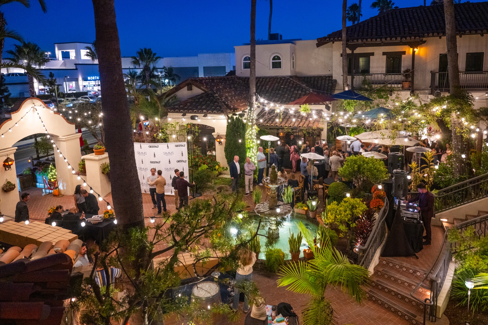 An evening private event in the Tin Roof Bistro courtyard at blue hour, string lights and palm trees