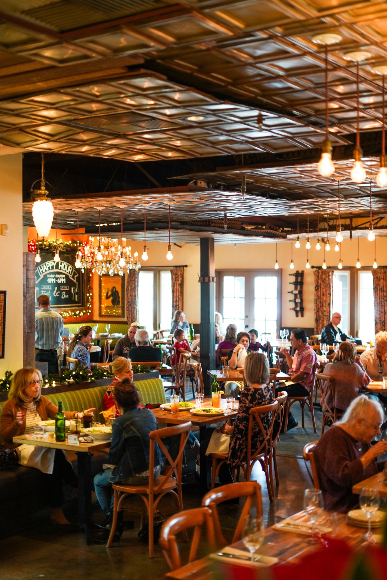 The bustling main dining room beneath the pressed-tin ceiling and Edison bulbs at Tin Roof Bistro
