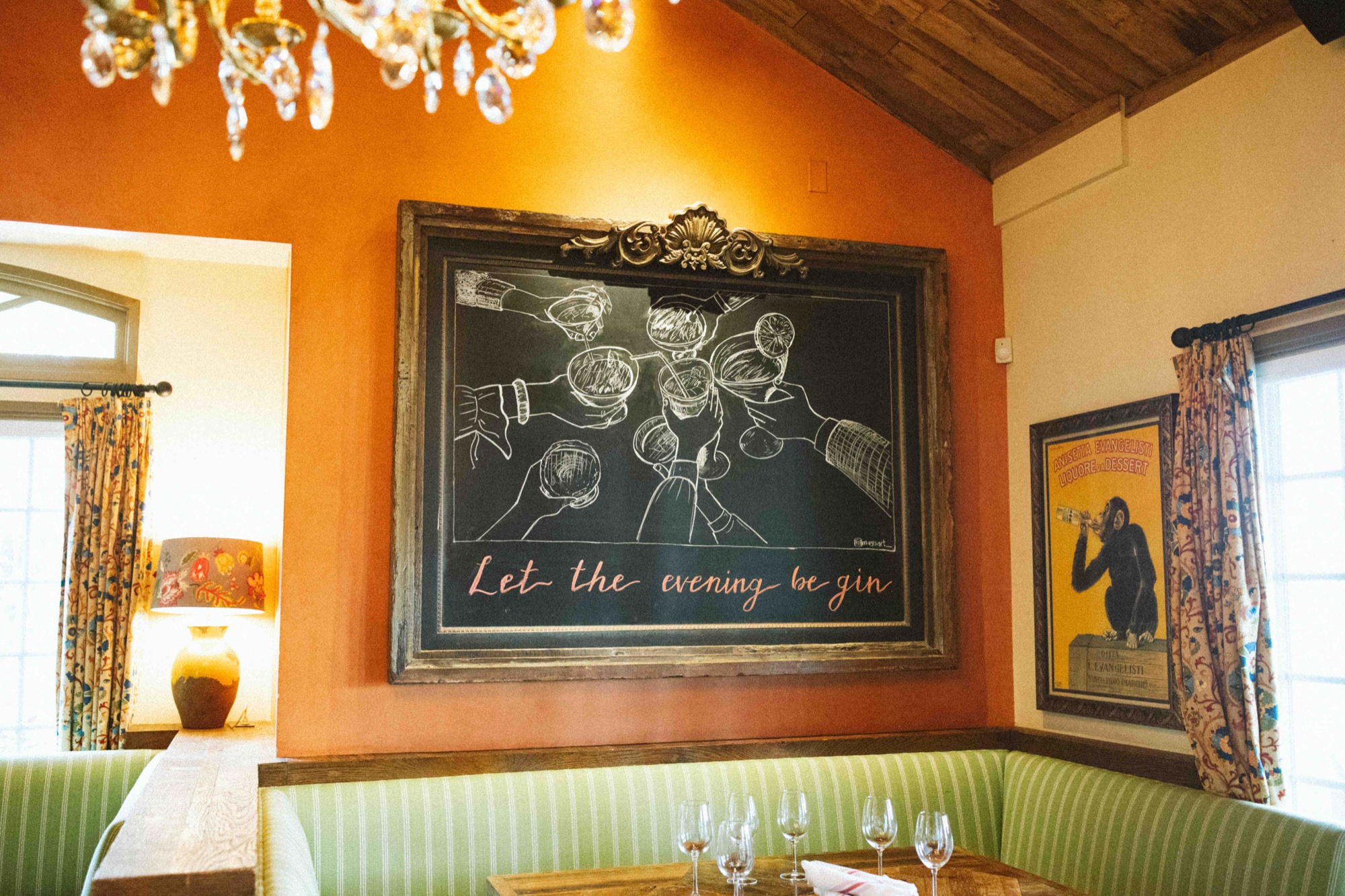 A cozy banquette nook with a chalkboard reading Let the Evening Be Gin at Tin Roof Bistro
